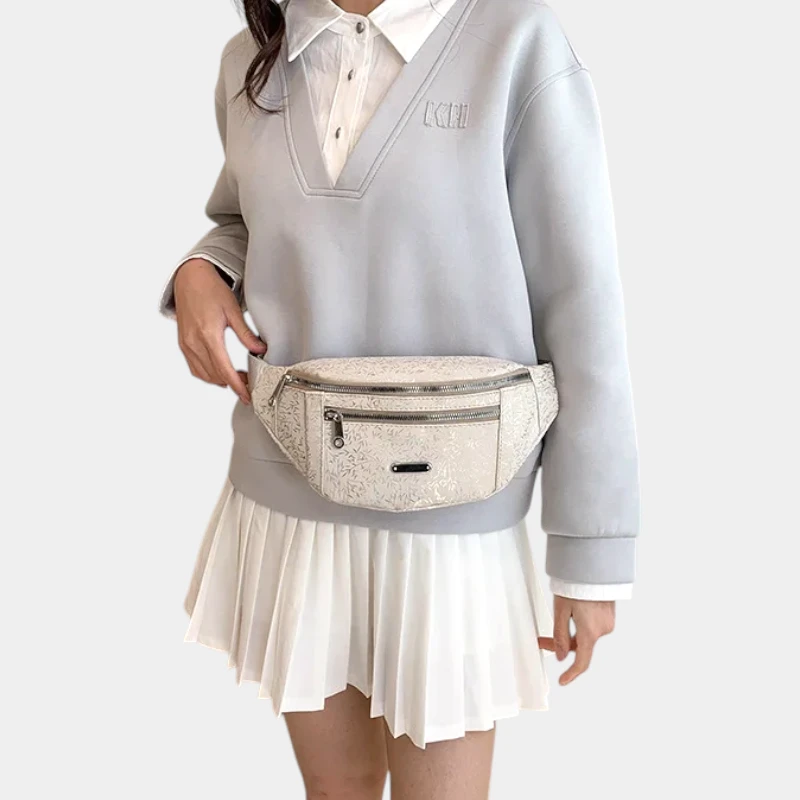 Sac banane demi-lune beige porté à la taille par une femme de face au style preppy