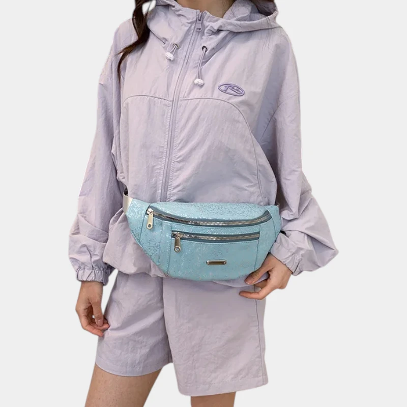 Sac banane demi-lune bleu ciel porté à la taille par une femme de face, tenu d'une main