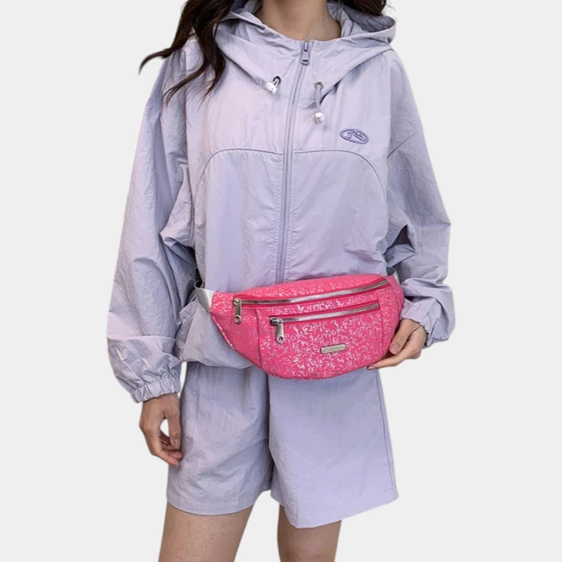 Sac banane demi-lune rose framboise porté à la taille par une femme de face, tenu d'une main