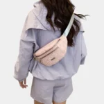 Sac Banane Imprimé Japonais Feuilles Argentées Sac banane demi-lune rose poudré porté en bandoulière dans le dos par une femme vue de dos