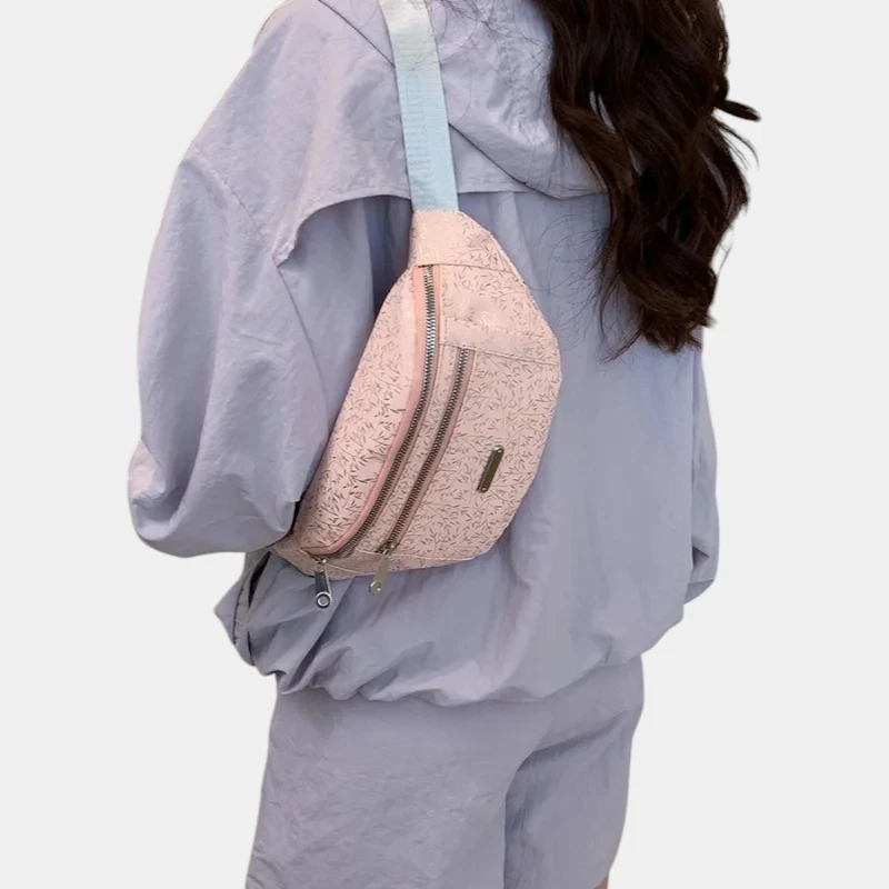 Sac banane demi-lune rose poudré porté en bandoulière dans le dos par une femme de trois-quarts