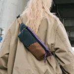 Sac Banane Rectangulaire Allongé Nylon Ripstop Déperlant Sac banane en nylon ripstop marron et gris ardoise porté en bandoulière dans le dos par une femme.