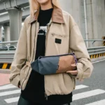 Sac Banane Rectangulaire Allongé Nylon Ripstop Déperlant Sac banane en nylon ripstop marron et gris ardoise tenu à deux mains, vu de face, cordelette tressée violette.