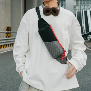Sac banane en nylon ripstop noir porté en bandoulière sur le torse par un homme, fermeture rouge bien visible.