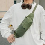 Sac Banane Rectangulaire Allongé Nylon Ripstop Déperlant Sac banane en nylon ripstop vert kaki porté en bandoulière sur le torse par un homme, vu de face.