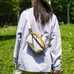 Sac banane en nylon froissé blanc porté en bandoulière dans le dos par une femme dans une prairie