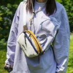 Sac banane en nylon froissé blanc à bande jaune porté en bandoulière sur la poitrine par une femme