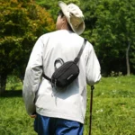 Sac banane en nylon froissé noir porté dans le dos par un homme en randonnée dans une prairie boisée