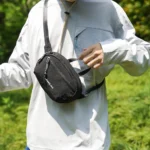 Sac banane en nylon froissé noir porté en bandoulière sur la poitrine par un homme en pleine nature