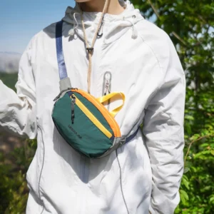 Sac banane en nylon froissé vert porté en bandoulière sur la poitrine par un homme en randonnée