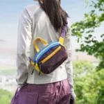 Sac banane en nylon froissé violet porté dans le dos par une femme en randonnée face au panorama