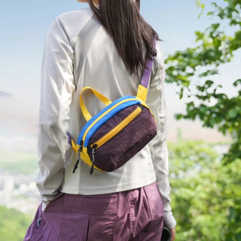 Sac banane en nylon froissé violet porté dans le dos par une femme en randonnée face au panorama