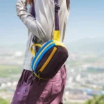 Sac banane en nylon froissé violet porté en bandoulière de profil par une femme en randonnée