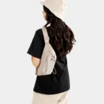Sac Banane Randonnée Poche Gourde Nylon Déperlant Sac banane en nylon beige porté en bandoulière dans le dos par une femme avec poche avant à cordon