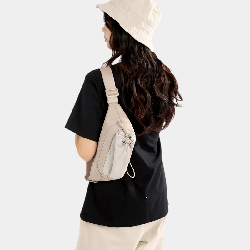 Sac banane en nylon beige porté en bandoulière dans le dos par une femme avec poche avant à cordon