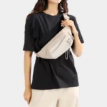 Sac Banane Randonnée Poche Gourde Nylon Déperlant Sac banane en nylon beige porté en bandoulière sur la poitrine par une femme, de face