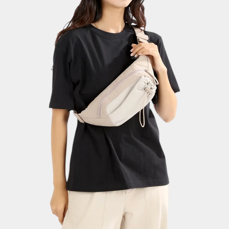 Sac banane en nylon beige porté en bandoulière sur la poitrine par une femme, de face