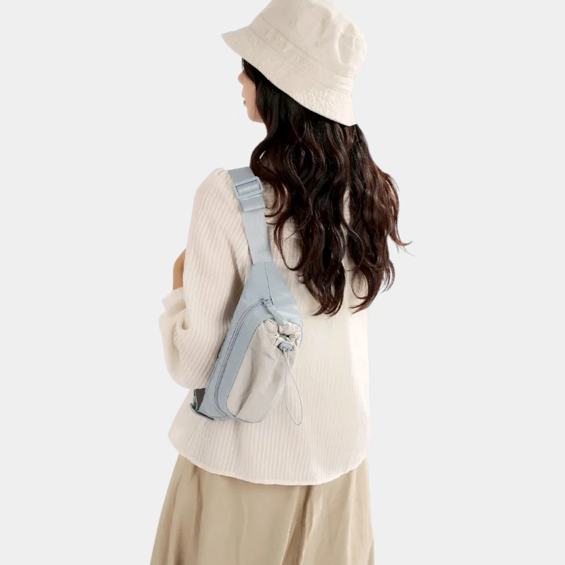 Sac banane en nylon bleu ciel porté en bandoulière dans le dos par une femme avec poche avant à cordon