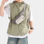 Sac Banane Randonnée Poche Gourde Nylon Déperlant Sac banane en nylon gris porté en bandoulière sur la poitrine par un homme avec poche avant à cordon
