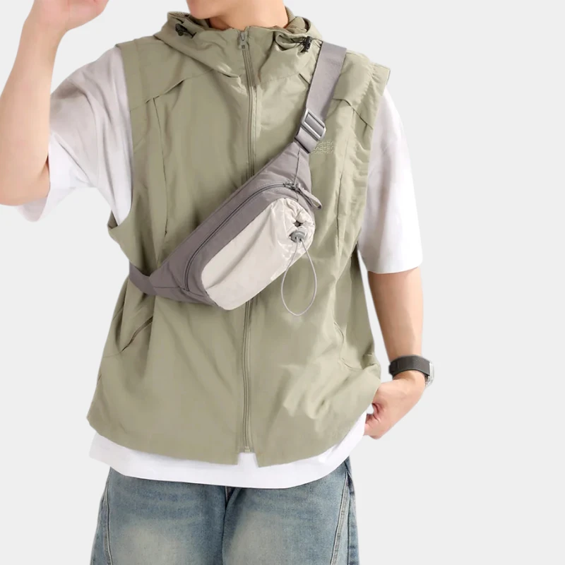 Sac banane en nylon gris porté en bandoulière sur la poitrine par un homme avec poche avant à cordon