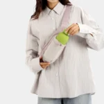 Sac Banane Randonnée Poche Gourde Nylon Déperlant Sac banane en nylon rose pâle porté en bandoulière par une femme qui glisse une gourde dans la poche avant