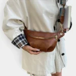 Sac banane camel porté en bandoulière croisée par une femme au style chic casual, avec une sangle ethnique colorée