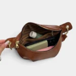 Sac banane en simili cuir camel ouvert, révélant une doublure chevronnée et des cosmétiques rangés à l'intérieur