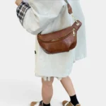 Sac banane en cuir cognac porté en bandoulière par une femme au style casual-chic, vu de dos