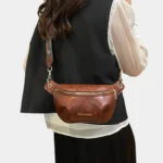 Sac banane simili cuir marron porté en bandoulière par une femme au style chic avec une sangle ethnique dorée