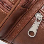 Sac banane en cuir marron, gros plan sur la tirette argentée de la fermeture éclair latérale