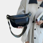 Sac banane simili cuir noir tenu à la main par une femme au style chic-casual, avec une sangle ethnique dorée et bleue