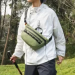 Sac banane vert kaki porté sur la poitrine par un randonneur tenant un bâton de marche