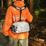 Sac banane en nylon gris clair porté dans le bas du dos avec son harnais de poitrine lors d'une randonnée en forêt