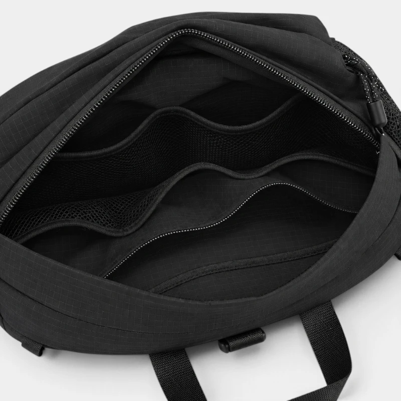 Sac banane en nylon ripstop noir ouvert sur son compartiment principal à poche zippée et poches en filet