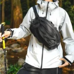Sac banane en nylon noir porté en bandoulière sur la poitrine par un homme lors d'une randonnée en forêt
