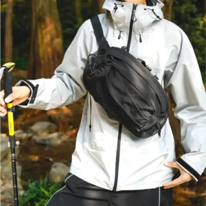 Sac banane en nylon noir porté en bandoulière sur la poitrine par un homme lors d'une randonnée en forêt