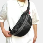 Grand Sac Banane Streetwear Nylon Poche Filet Sac banane noir porté en bandoulière sur le torse par un homme de face avec cordon élastique croisé