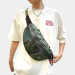 Grand Sac Banane Streetwear Nylon Poche Filet Sac banane vert kaki porté en bandoulière sur le torse par un homme de face avec poche avant en filet