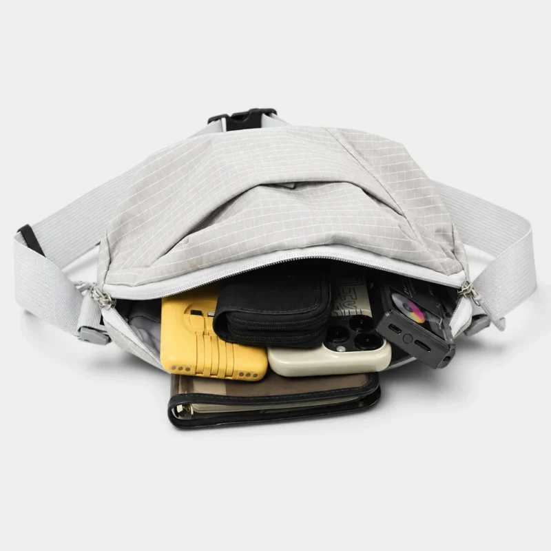 Sac banane gris clair à quadrillage ouvert vu de dessus avec un smartphone et un portefeuille rangés dans la poche principale