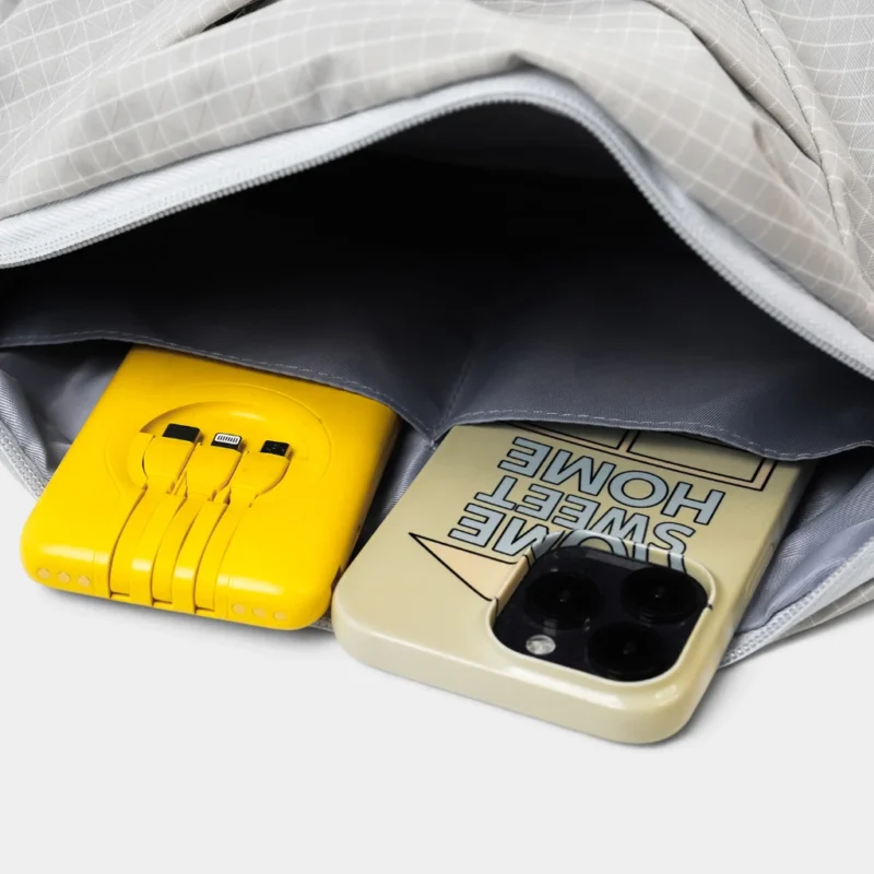 Sac banane gris clair ouvert en gros plan sur sa poche intérieure plaquée avec un smartphone et une batterie externe