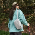 Sac banane gris clair à quadrillage porté en bandoulière dans le dos par une femme en randonnée en forêt