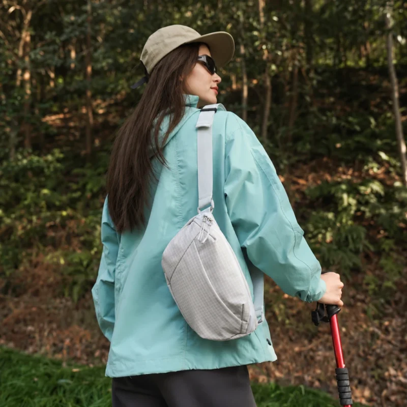 Sac banane gris clair à quadrillage porté en bandoulière dans le dos par une femme en randonnée en forêt