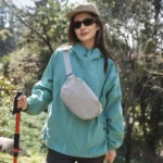 Sac banane gris clair à quadrillage porté en bandoulière sur la poitrine par une femme lors d'une randonnée en sous-bois