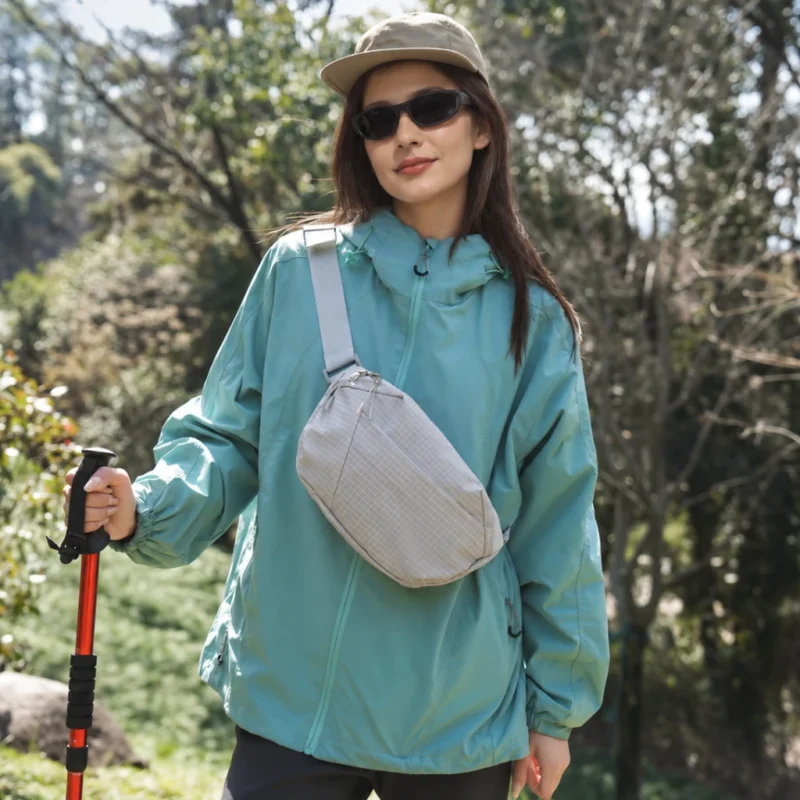 Sac banane gris clair à quadrillage porté en bandoulière sur la poitrine par une femme lors d'une randonnée en sous-bois