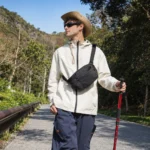Sac banane noir à quadrillage porté en bandoulière sur la poitrine par un homme lors d'une randonnée sur une petite route