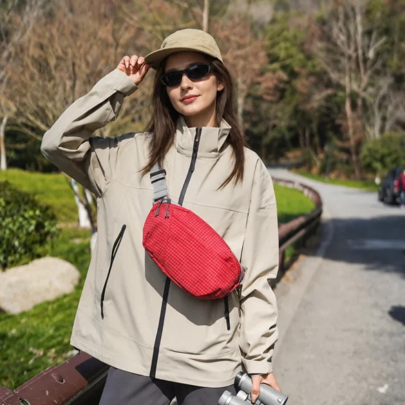 Sac banane rouge à quadrillage porté en bandoulière sur la poitrine par une femme lors d'une balade en plein air