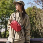 Sac banane rouge à quadrillage porté en bandoulière sur la poitrine par une femme lors d'une promenade en forêt