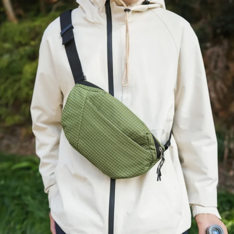 Sac banane vert kaki à fin quadrillage blanc porté en bandoulière sur la poitrine lors d'une marche en forêt