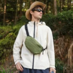 Sac banane vert kaki à quadrillage porté en bandoulière sur la poitrine par un homme lors d'une randonnée en forêt