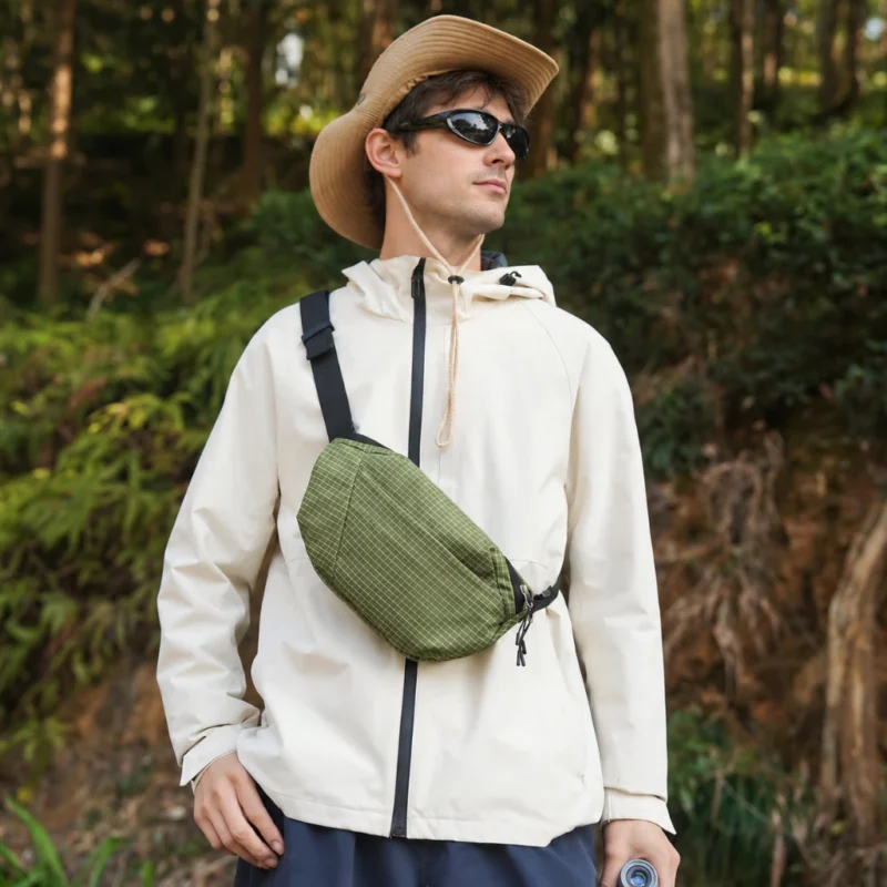 Sac banane vert kaki à quadrillage porté en bandoulière sur la poitrine par un homme lors d'une randonnée en forêt